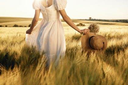 Beautiful young bride in white dress is on the agricultural field at sunny day
