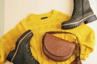 Flat lay of woman's yellow sweater and brown bag, pair of boots on neutral beige background